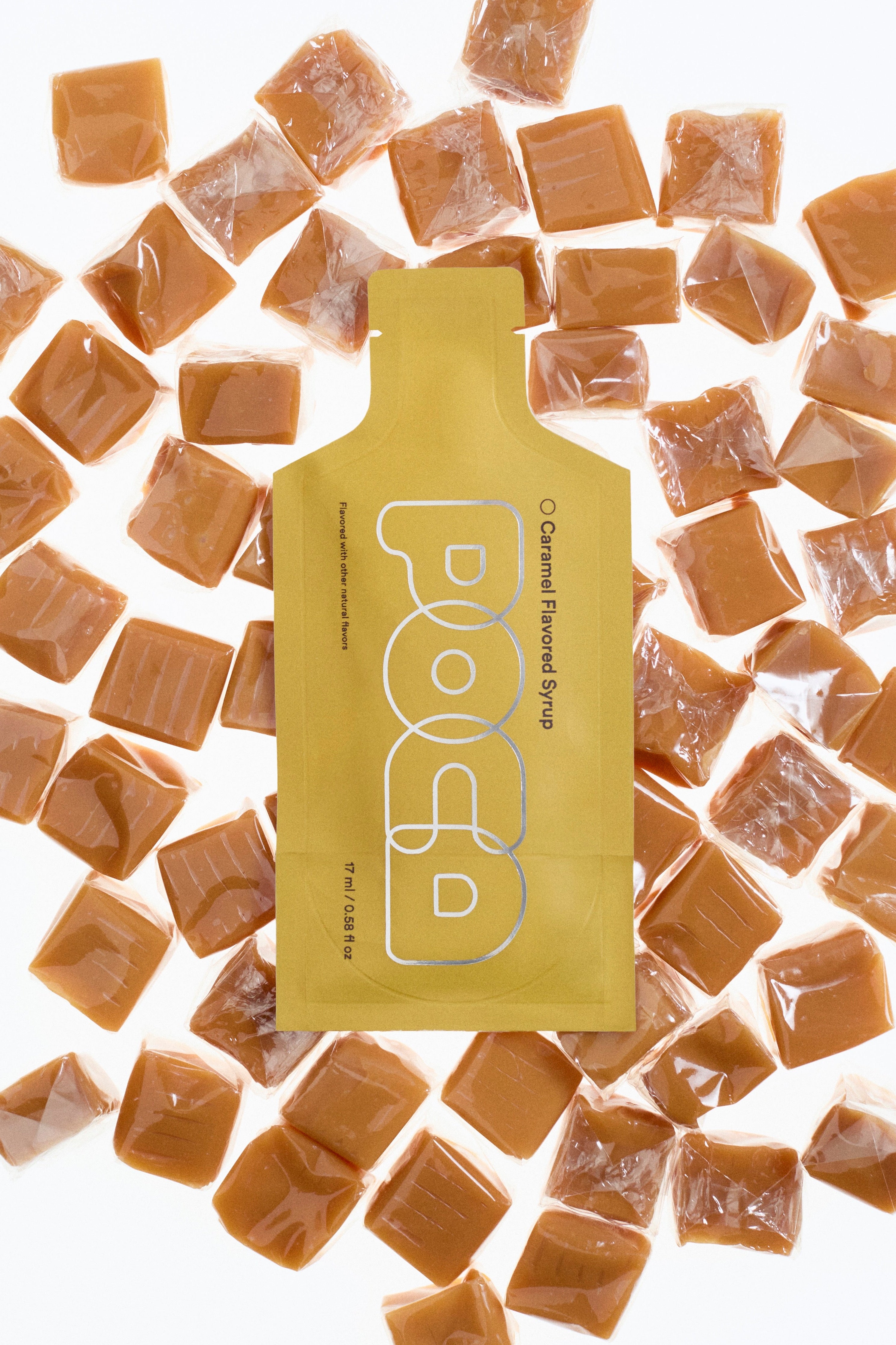 Packaging of caramel-flavored syrup surrounded by caramel cubes on a white background.