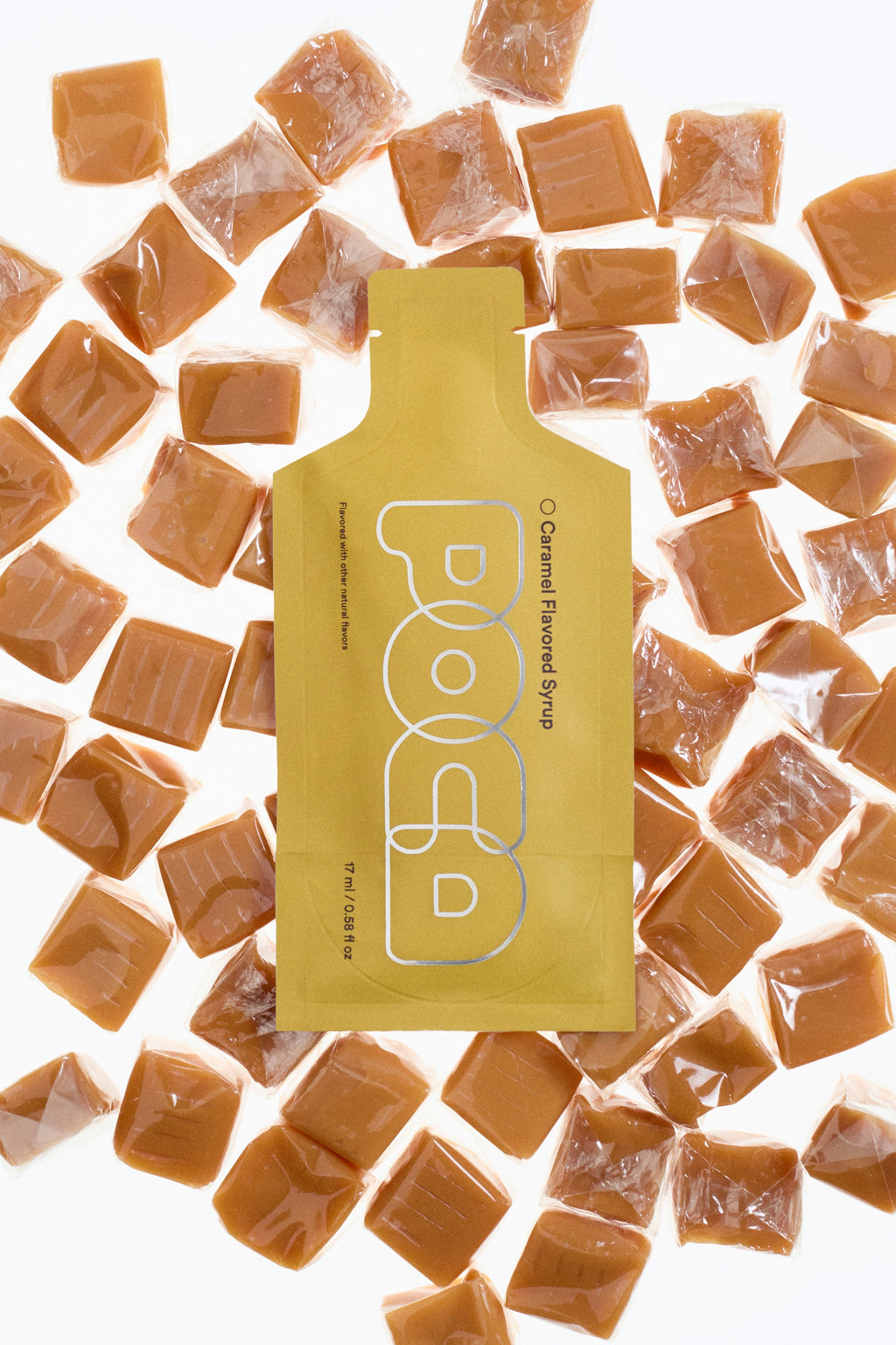 Packaging of caramel-flavored syrup surrounded by caramel cubes on a white background.