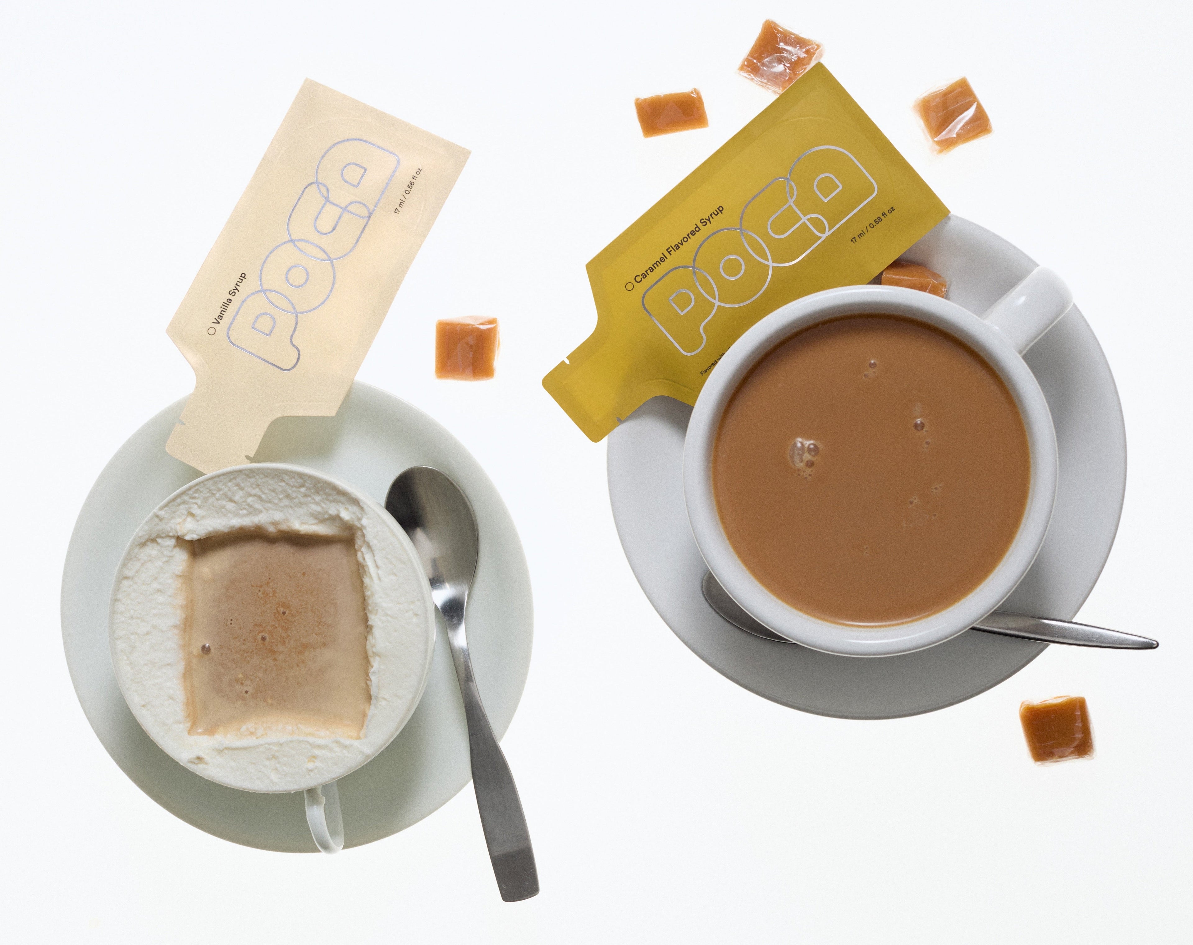 Two cups of coffee with milk foam along the edge and two poca packets on the side.