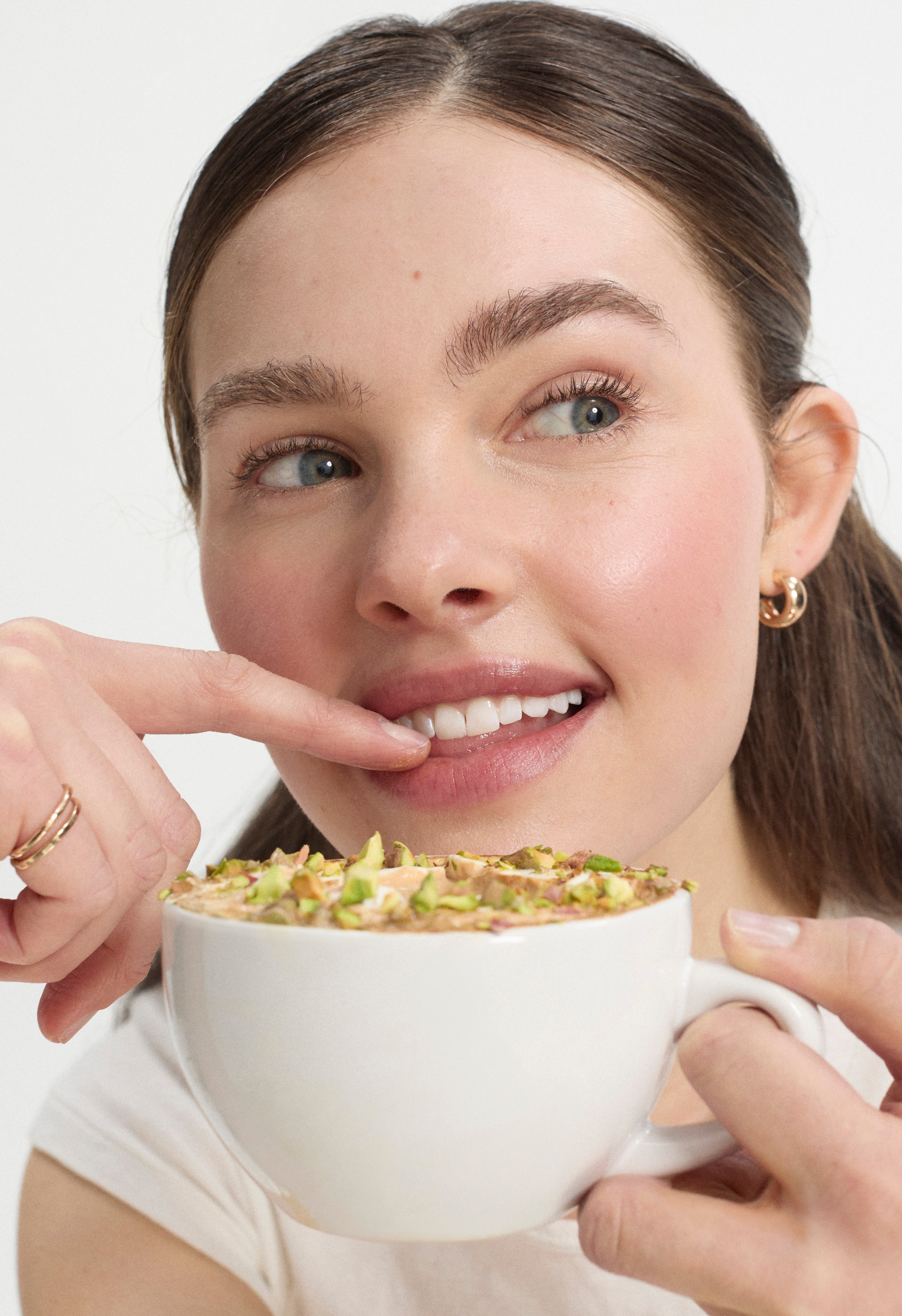 Woman holding a cappuccino topped with pistachios pointing to it with her finger.