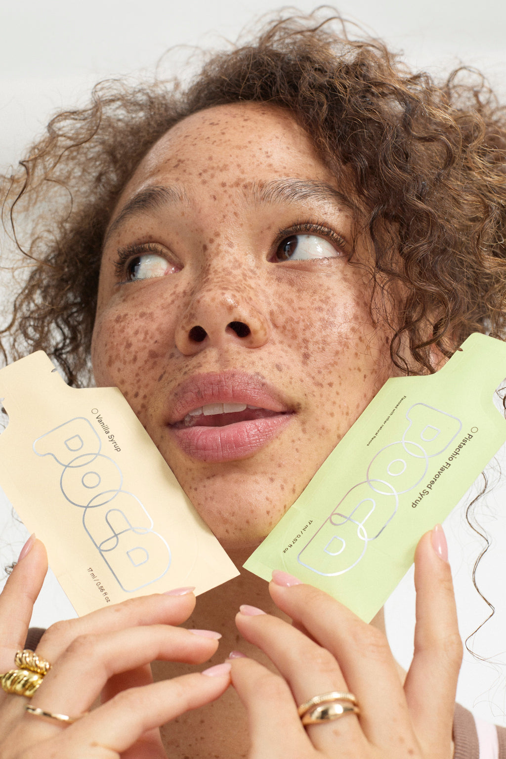 Woman with curly hair holding two POCAs up to her face like skincare products.